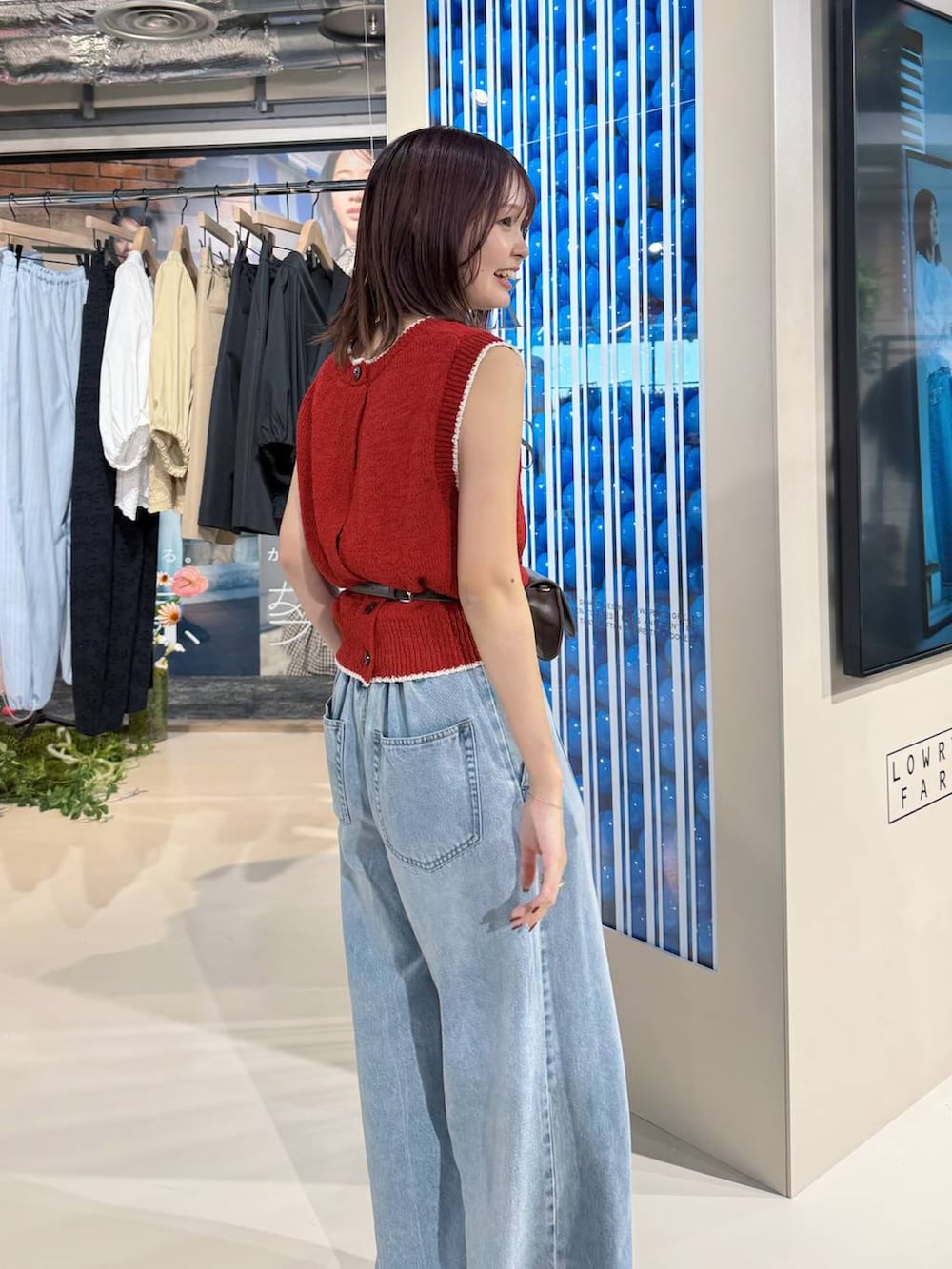 ブルー系のデニムパンツ、ブラック系のサンダル、レッド系のベストを着用したレディースの春コーディネートの2枚目の写真