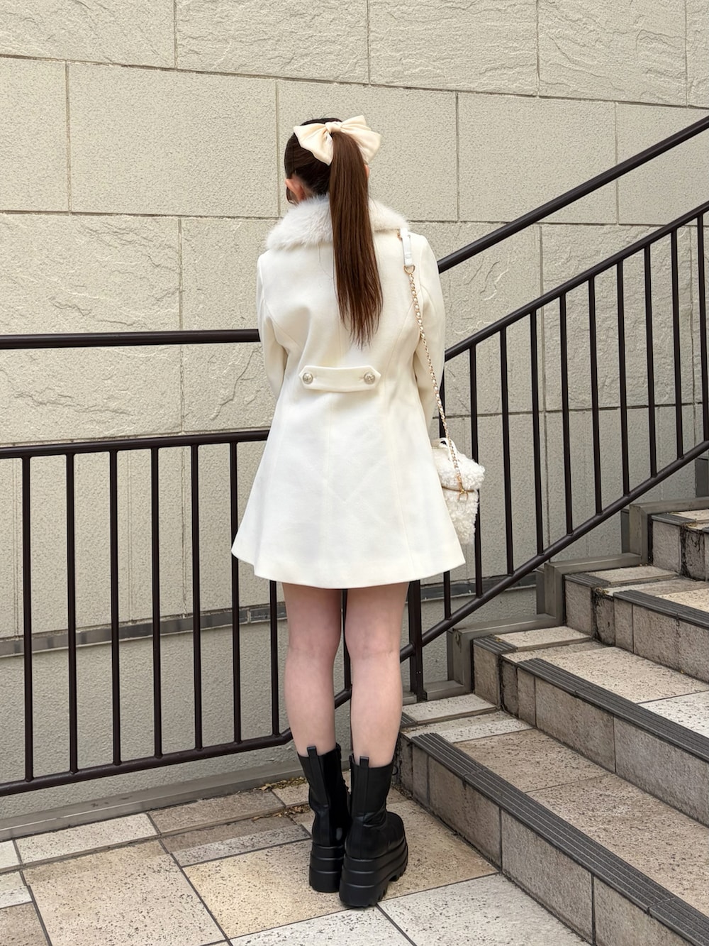 ホワイト系のステンカラーコート、ホワイト系のショルダーバッグ、ブラック系のブーツを着用したレディースの冬コーディネートの3枚目の写真