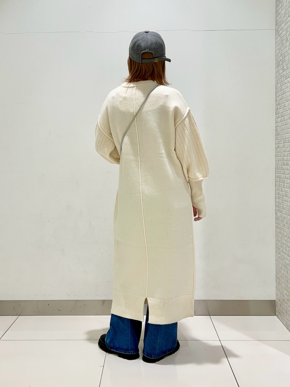 シルバー系のショルダーバッグ、ホワイト系のワンピース、ブルー系のデニムパンツを着用したレディースの冬コーディネートの9枚目の写真