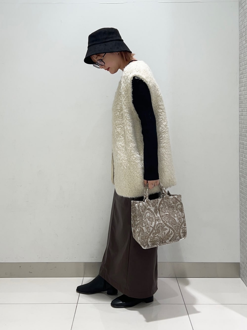 ベージュ系のトートバッグ、ブラック系のニット/セーター、ブラウン系のスカートを着用したレディースの秋コーディネートの3枚目の写真