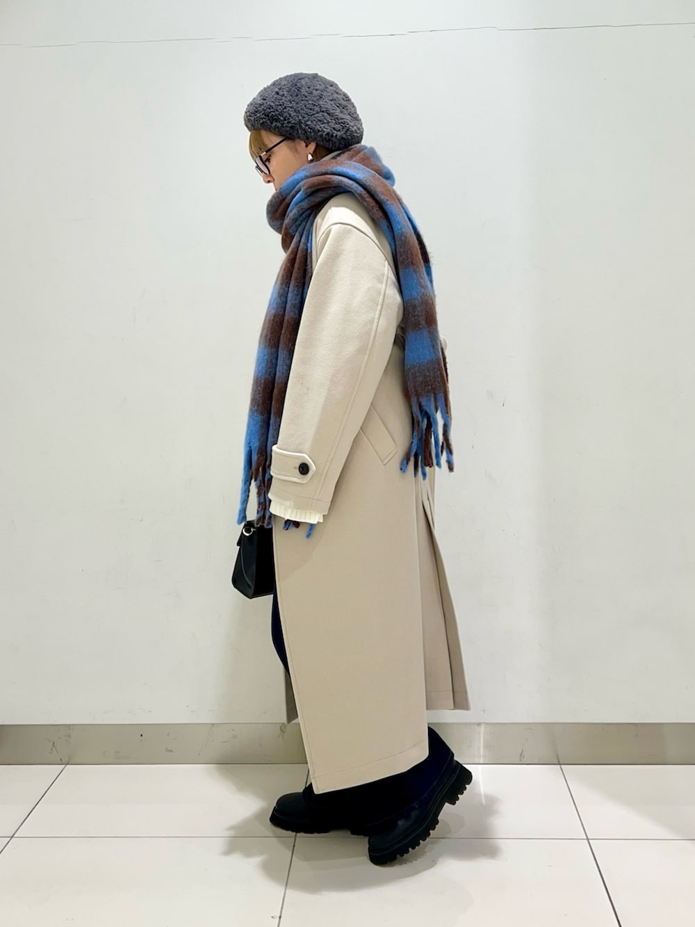 ベージュ系のステンカラーコート、ブルー系のデニムパンツ、ブラック系のショルダーバッグを着用したレディースの冬コーディネートの3枚目の写真