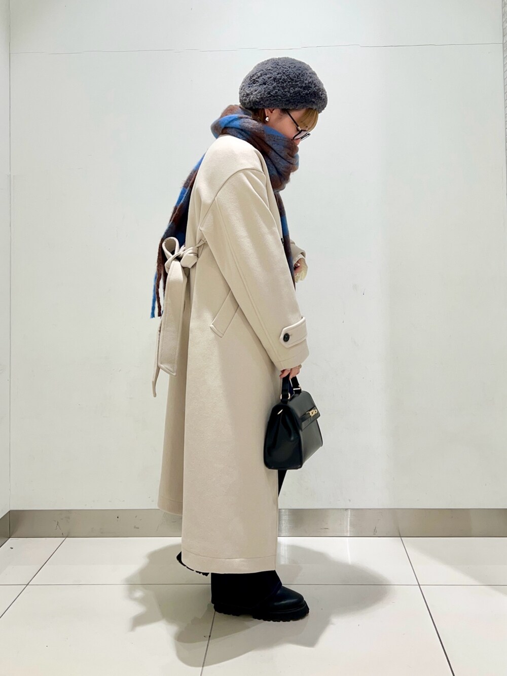 ベージュ系のステンカラーコート、ブルー系のデニムパンツ、ブラック系のショルダーバッグを着用したレディースの冬コーディネートの5枚目の写真