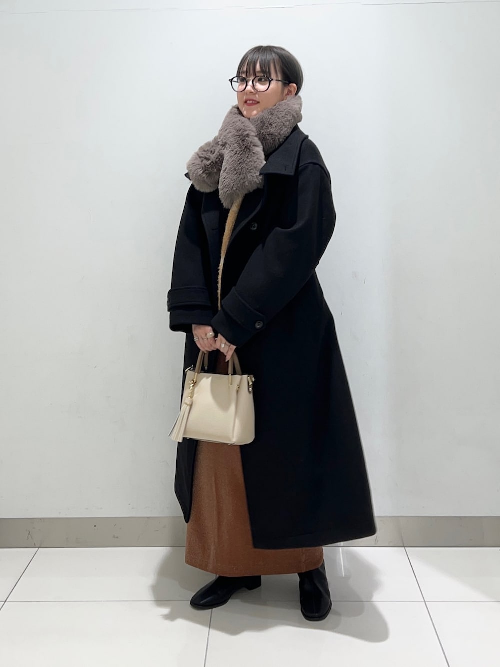 ブラック系のブーツ、ホワイト系のトートバッグ、ブラウン系のスカートを着用したレディースの秋コーディネートの6枚目の写真