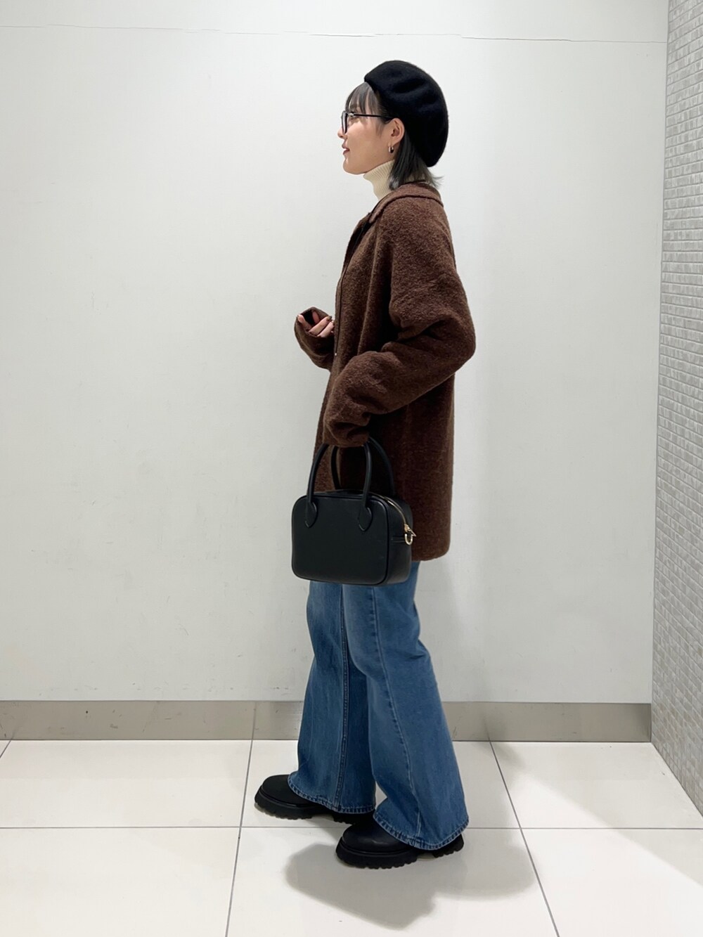 ブラック系のブーツ、ブルー系のデニムパンツ、ブラック系のボストンバッグを着用したレディースの秋コーディネートの3枚目の写真
