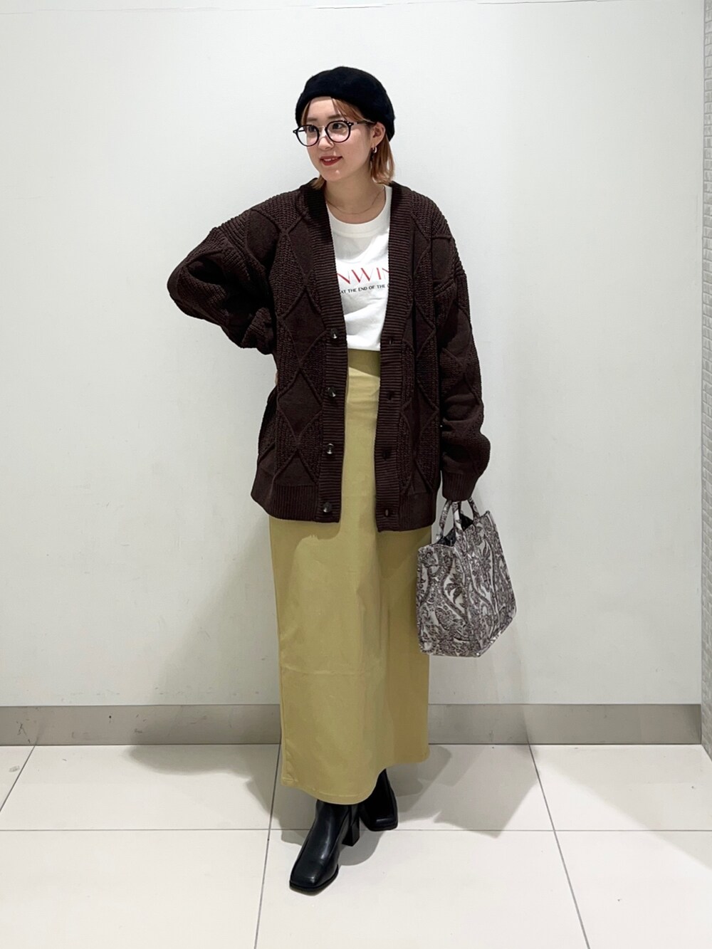 ベージュ系のトートバッグ、ブラック系のブーツ、イエロー系のスカートを着用したレディースの秋コーディネートの2枚目の写真