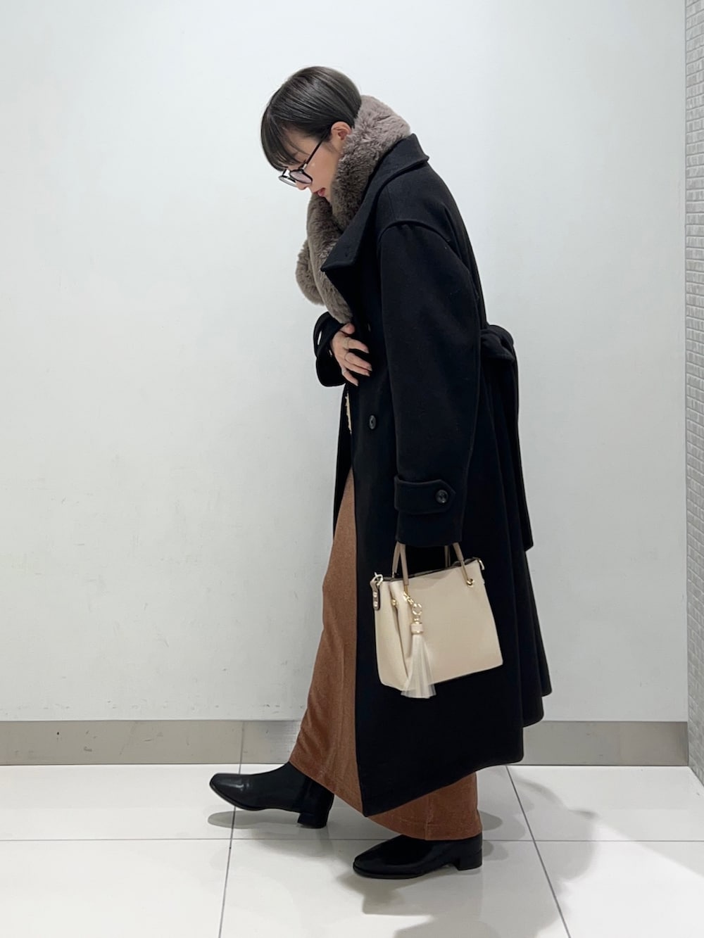 ブラック系のブーツ、ホワイト系のトートバッグ、ブラウン系のスカートを着用したレディースの秋コーディネートの3枚目の写真