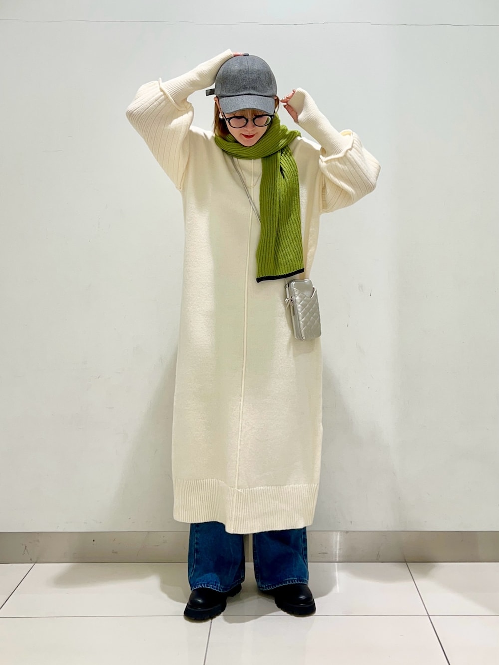 シルバー系のショルダーバッグ、ホワイト系のワンピース、ブルー系のデニムパンツを着用したレディースの冬コーディネートの6枚目の写真