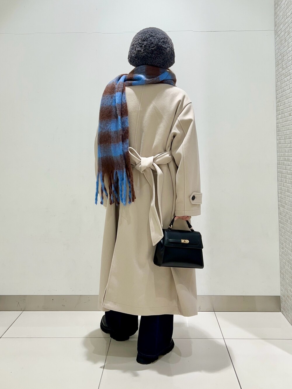 ベージュ系のステンカラーコート、ブルー系のデニムパンツ、ブラック系のショルダーバッグを着用したレディースの冬コーディネートの4枚目の写真