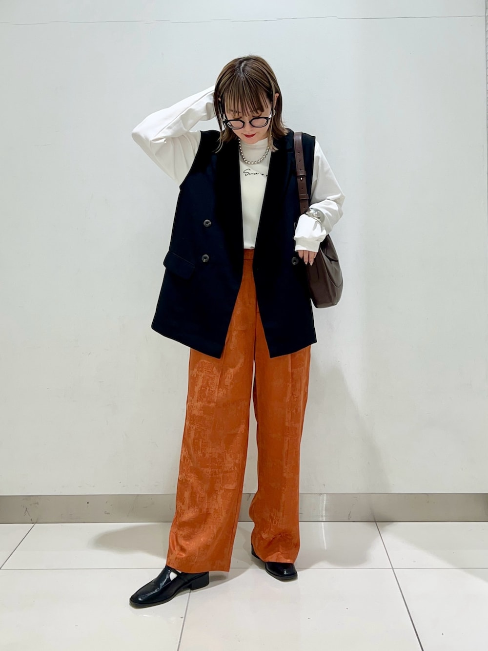 ブラウン系のショルダーバッグ、ブラック系のその他アウター、オレンジ系のその他パンツを着用したレディースの春コーディネートの2枚目の写真