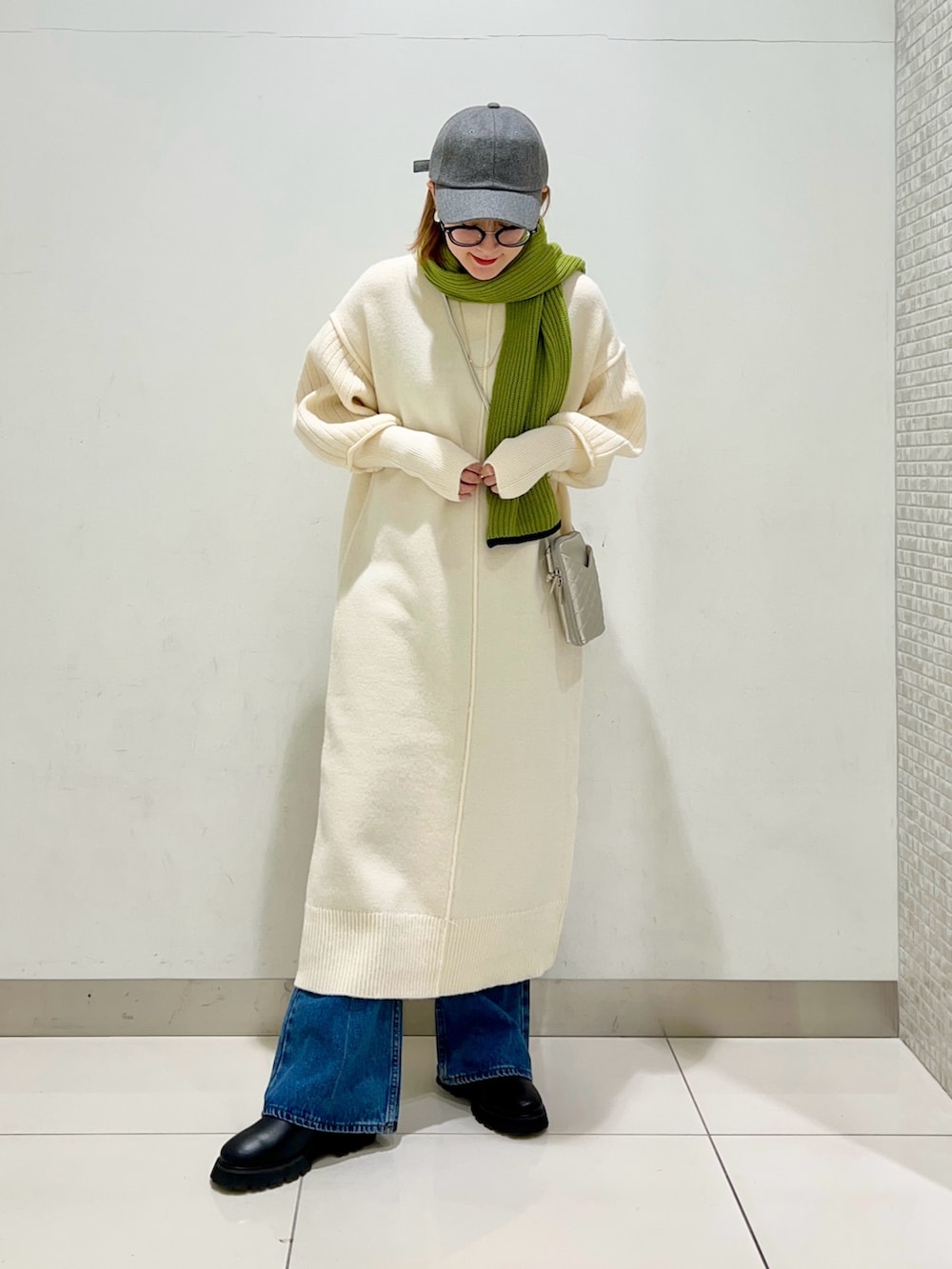 シルバー系のショルダーバッグ、ホワイト系のワンピース、ブルー系のデニムパンツを着用したレディースの冬コーディネートの2枚目の写真