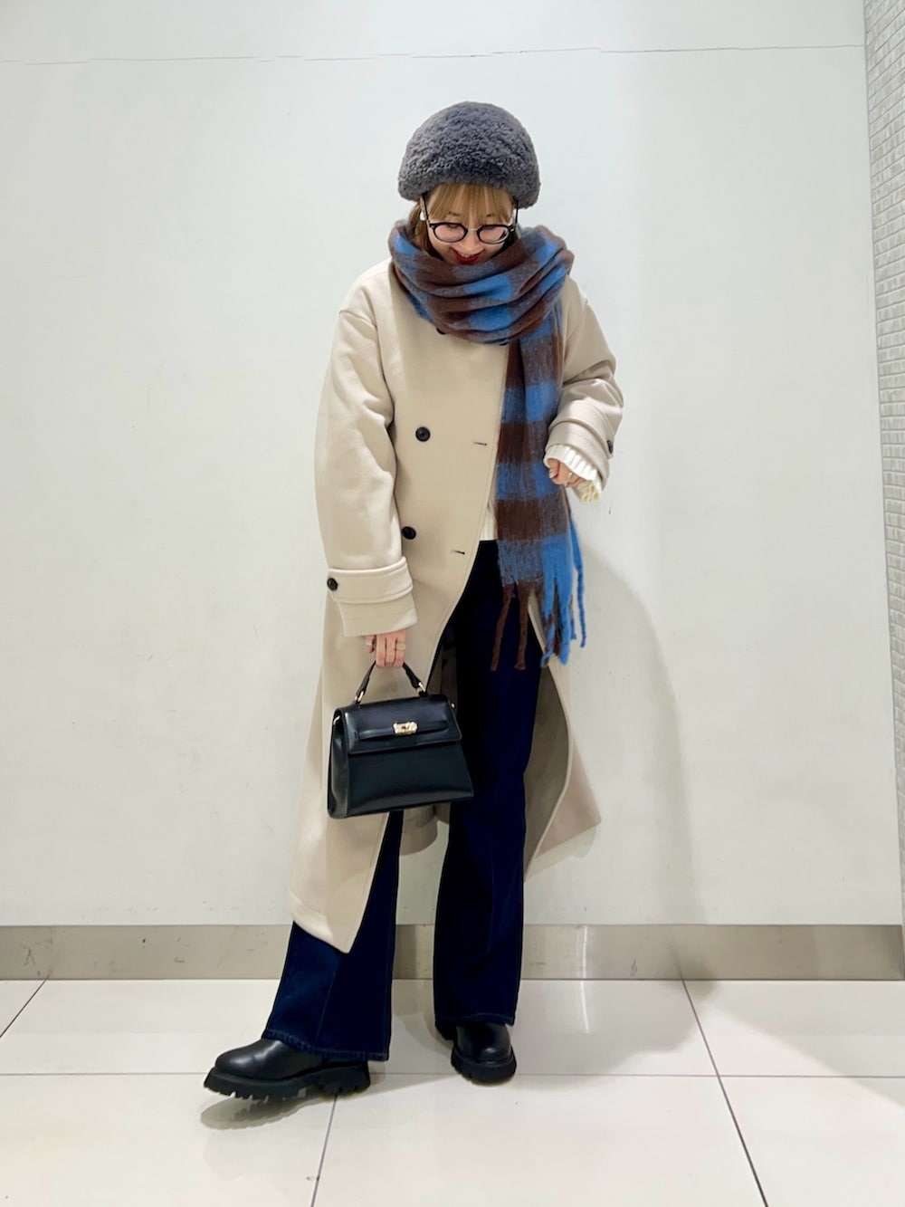 ベージュ系のステンカラーコート、ブルー系のデニムパンツ、ブラック系のショルダーバッグを着用したレディースの冬コーディネートの2枚目の写真