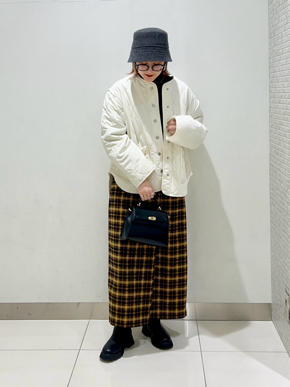 ホワイト系のジャケット/アウター、ブラック系のニット/セーター、イエロー系のスカートを着用したレディースの冬コーディネートの2枚目の写真