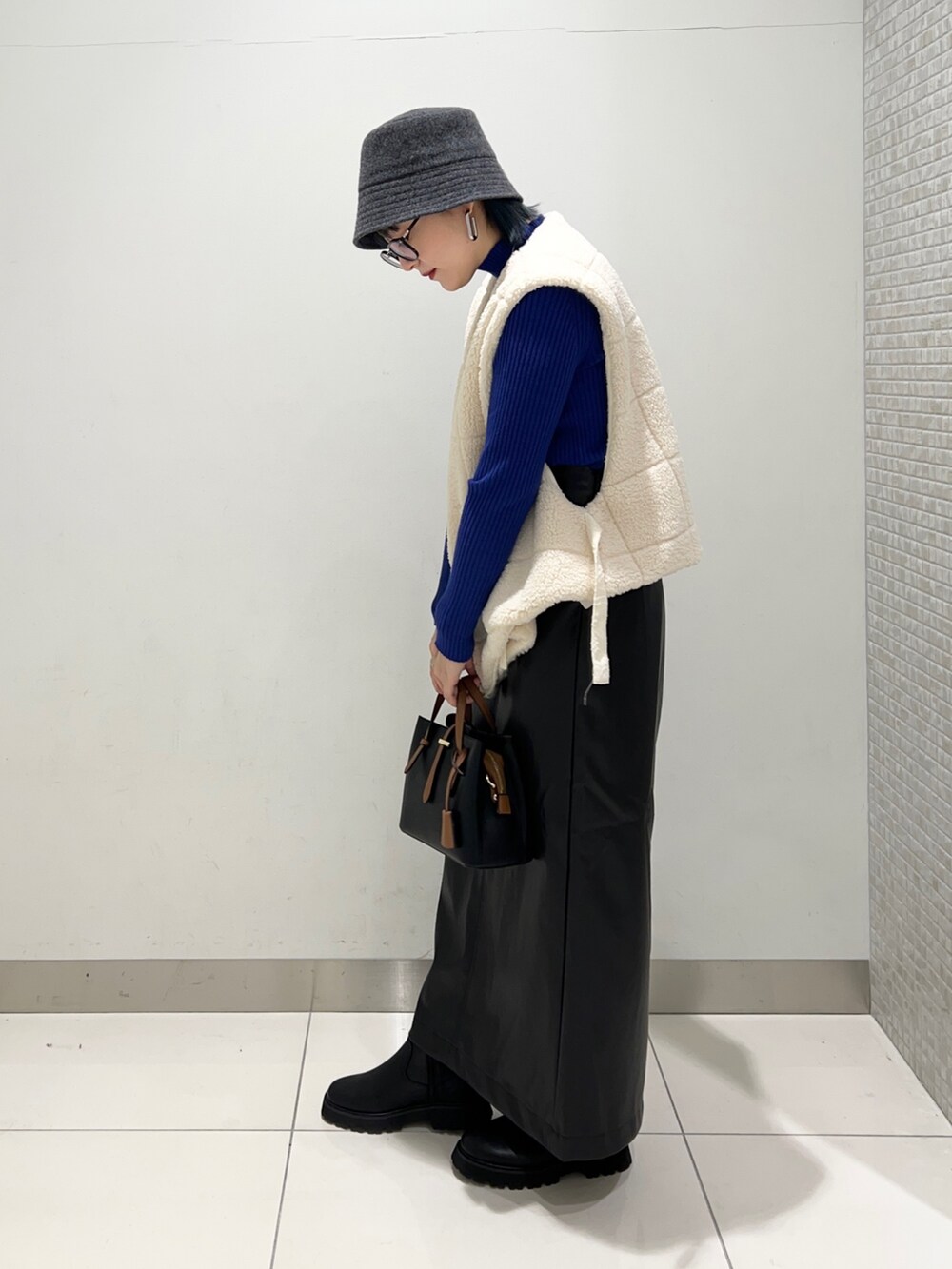 ホワイト系のベスト、ブラック系のスカート、ブルー系のニット/セーターを着用したレディースの秋コーディネートの3枚目の写真