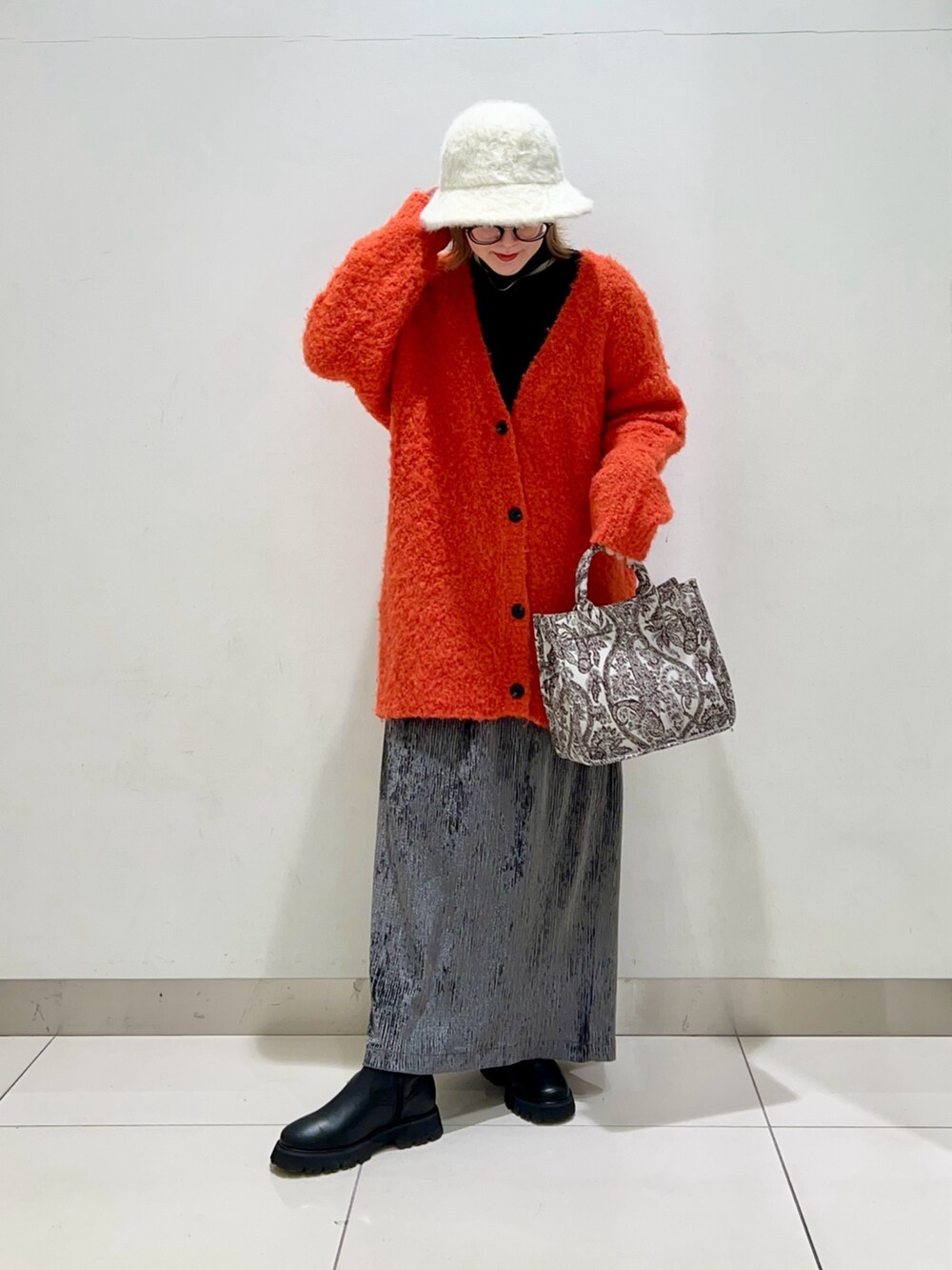 ブラック系のニット/セーター、オレンジ系のカーディガン/ボレロ、ブラウン系のトートバッグを着用したレディースの冬コーディネートの2枚目の写真