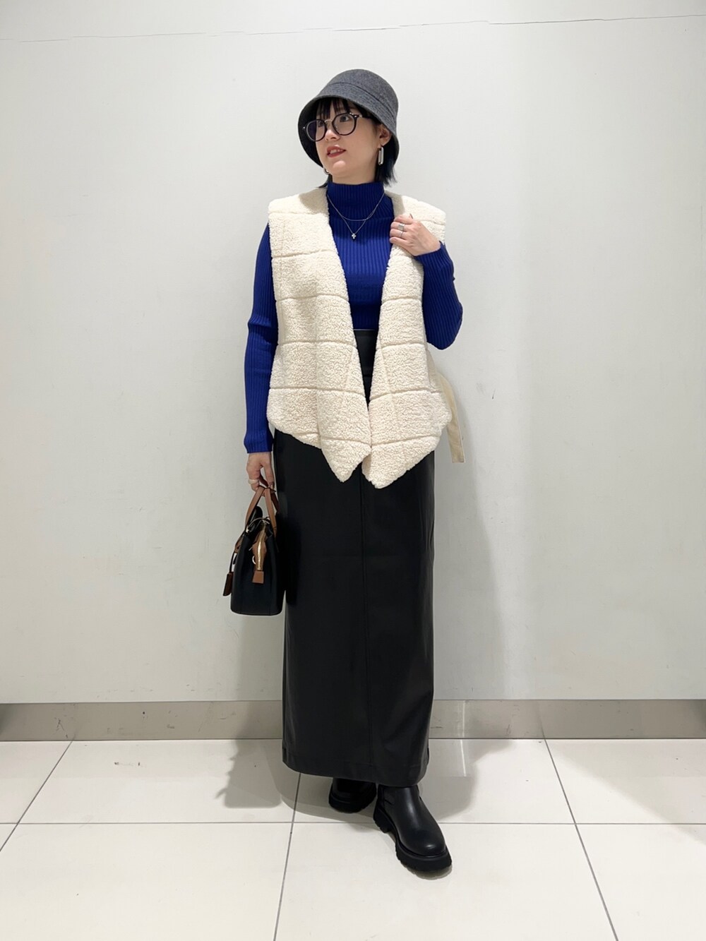 ホワイト系のベスト、ブラック系のスカート、ブルー系のニット/セーターを着用したレディースの秋コーディネートの6枚目の写真