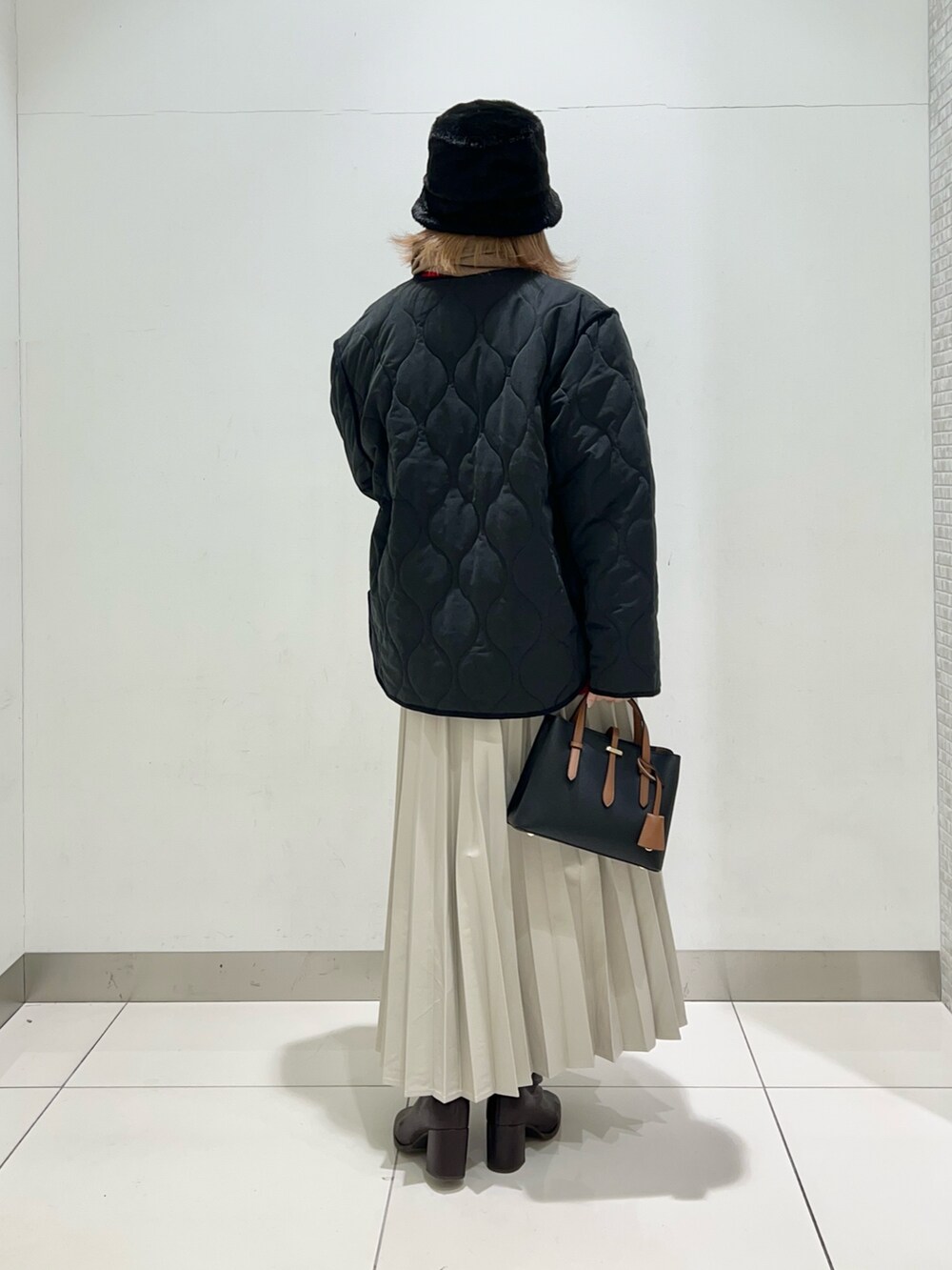 ブラウン系のブーツ、ベージュ系のスカート、ブラック系のハンドバッグを着用したレディースの冬コーディネートの6枚目の写真