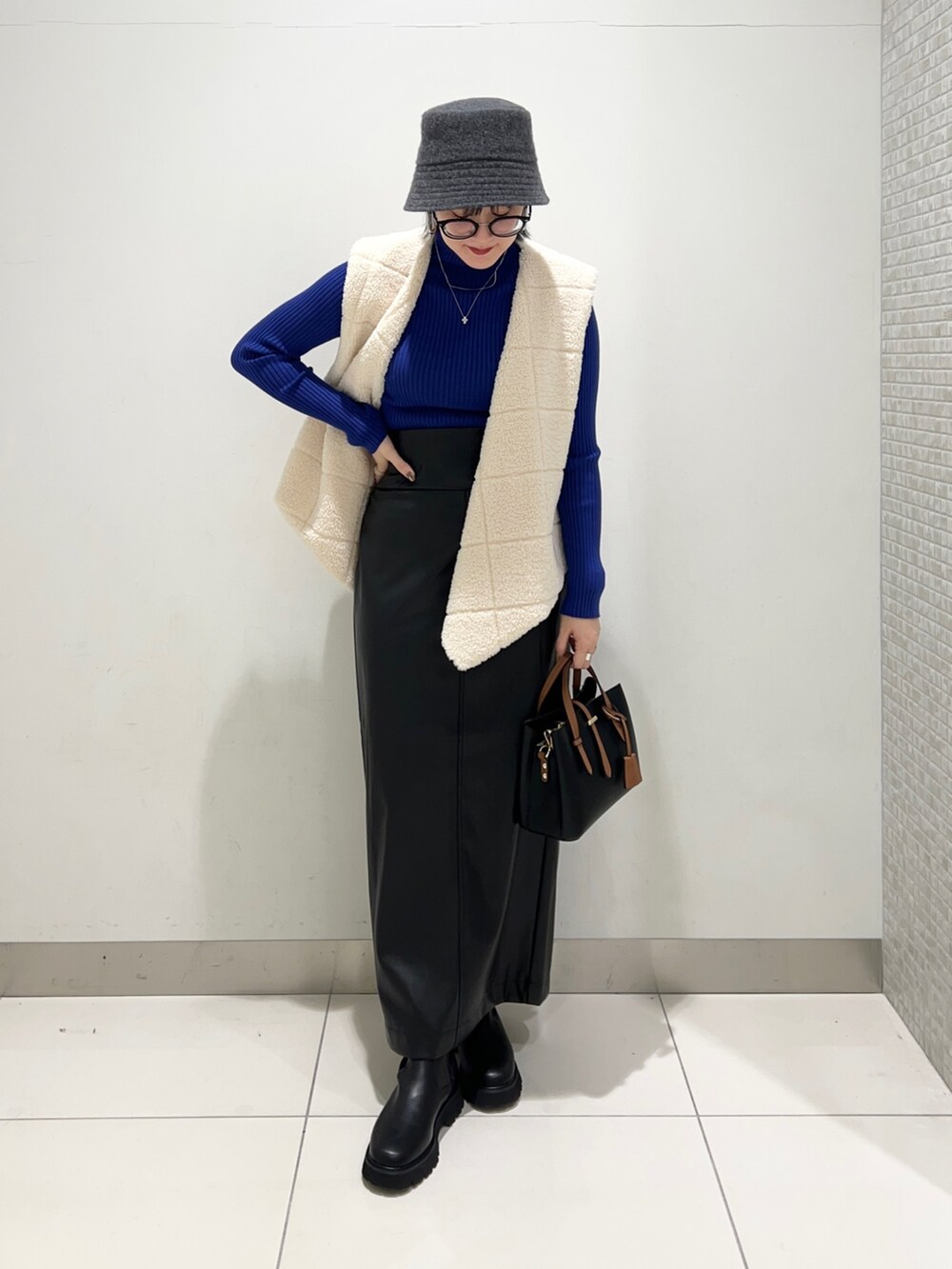 ホワイト系のベスト、ブラック系のスカート、ブルー系のニット/セーターを着用したレディースの秋コーディネートの2枚目の写真