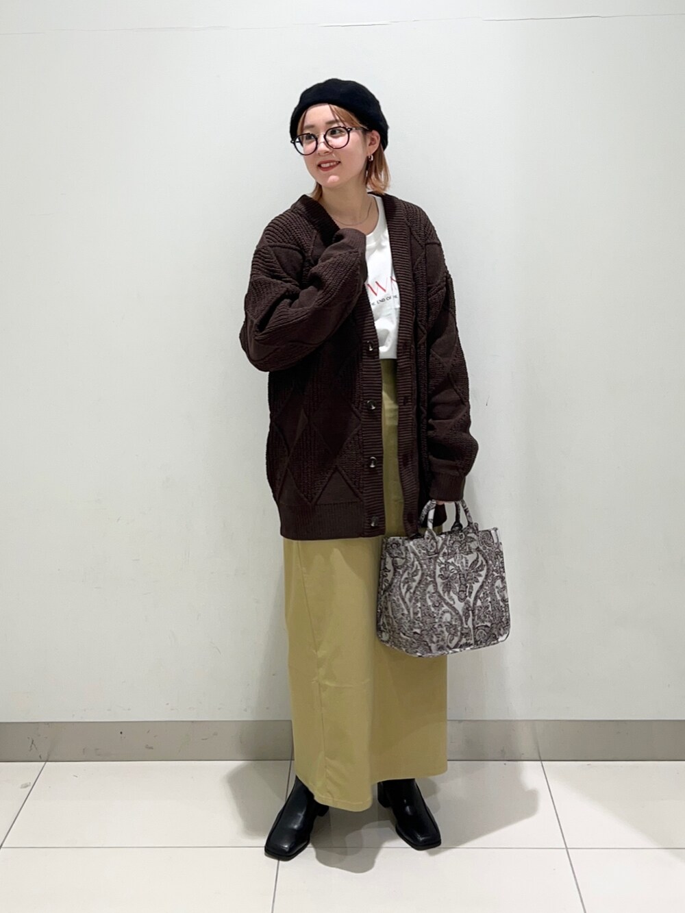 ベージュ系のトートバッグ、ブラック系のブーツ、イエロー系のスカートを着用したレディースの秋コーディネートの6枚目の写真