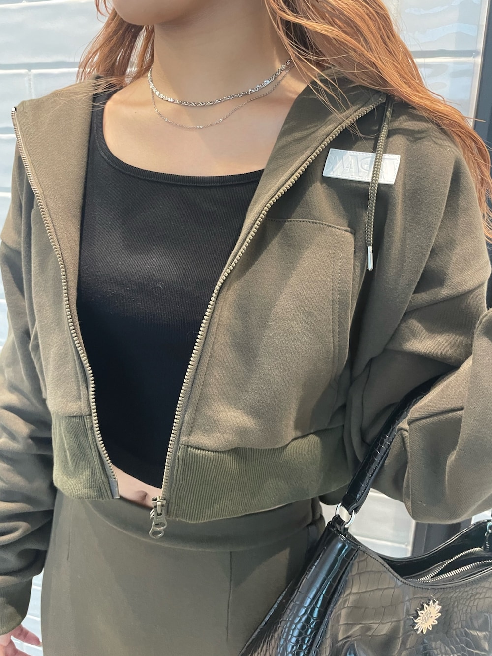 グリーン系のセットアップ、ブラック系のハンドバッグ、ブラック系のブーツを着用したレディースの秋コーディネートの3枚目の写真