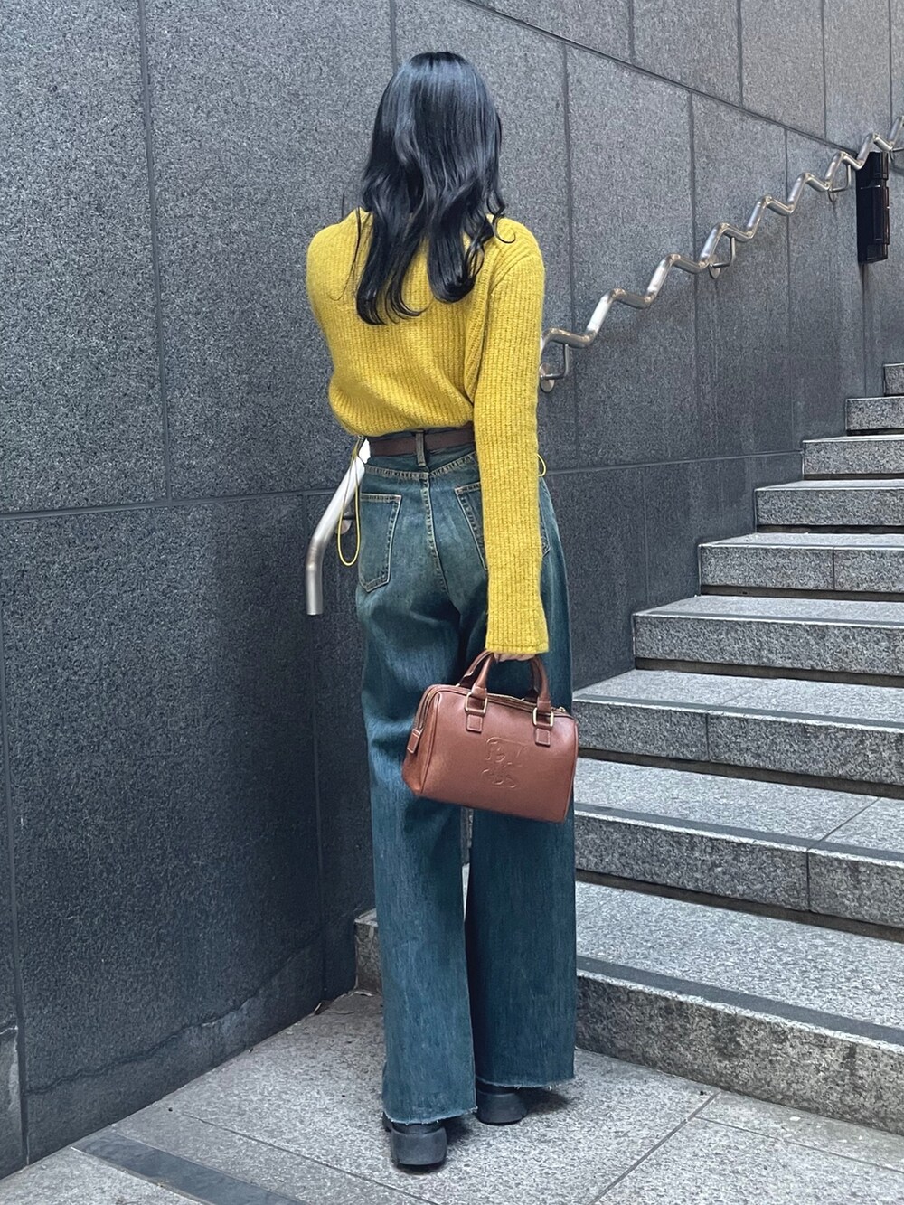 イエロー系のニット/セーター、ブルー系のデニムパンツ、ブラウン系のボストンバッグを着用したレディースの秋コーディネートの2枚目の写真