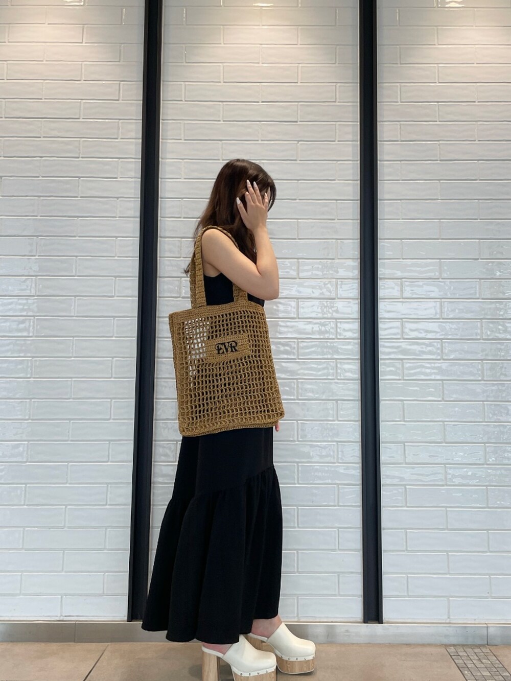 ブラック系のワンピース、ベージュ系のトートバッグ、ホワイト系のサンダルを着用したレディースの夏コーディネートの2枚目の写真