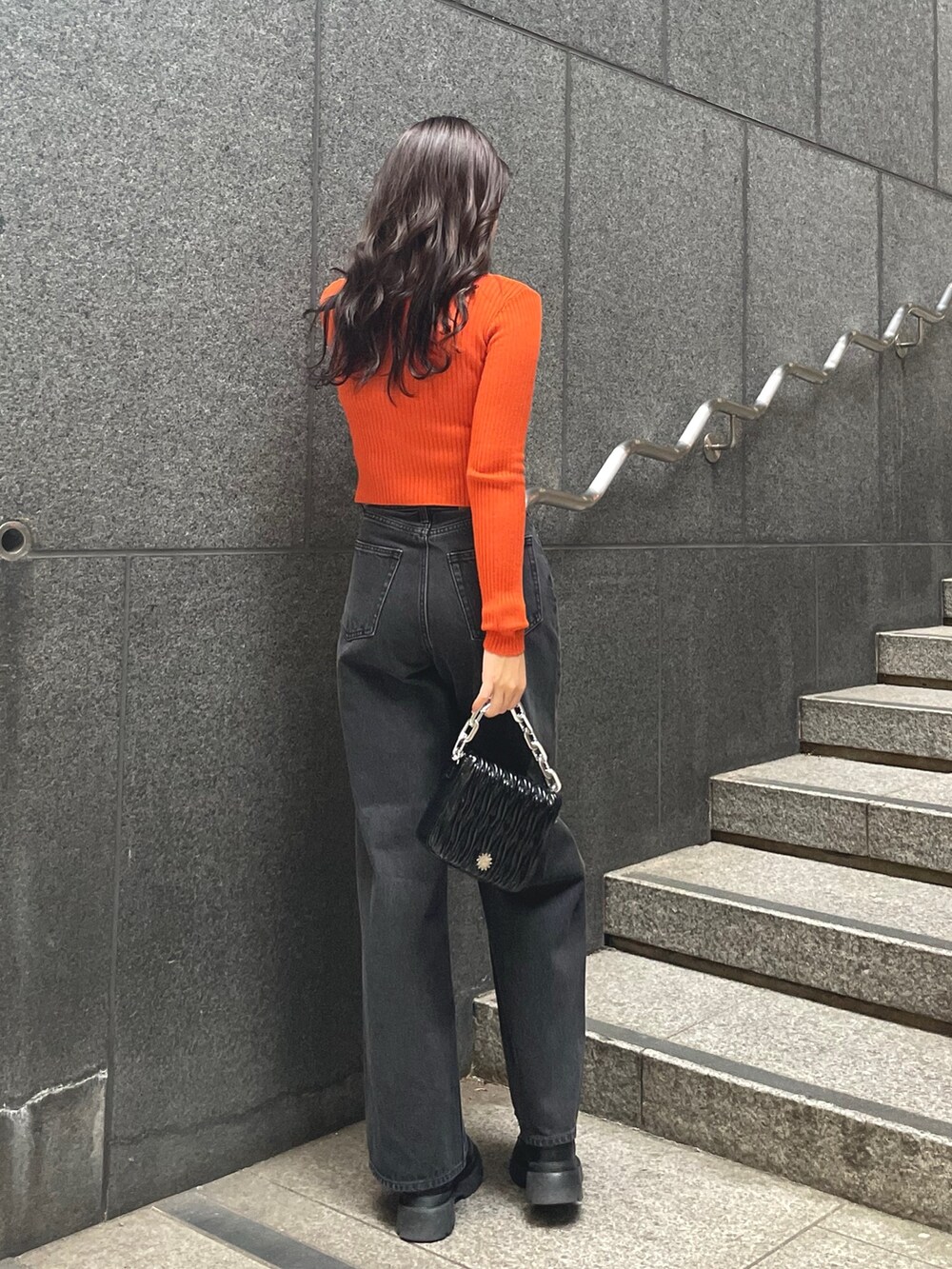 オレンジ系のニット/セーター、ブラック系のデニムパンツ、ブラック系のショルダーバッグを着用したレディースの秋コーディネートの2枚目の写真