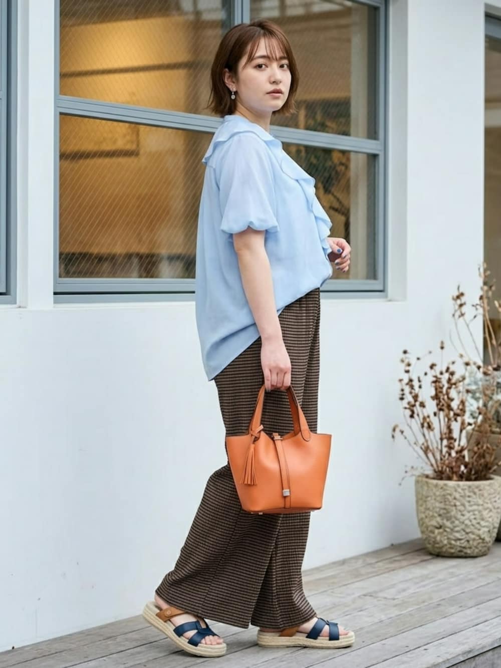 オレンジ系のトートバッグ、ブルー系のシャツ/ブラウス、ブラウン系のパンツを着用したレディースの夏コーディネートの6枚目の写真
