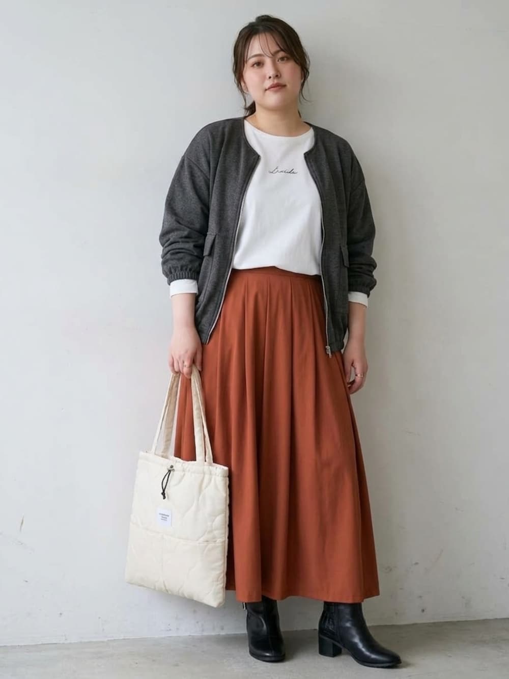 ブラウン系のスカート、ホワイト系のTシャツ/カットソー、ブラック系のブーツを着用したレディースの秋コーディネートの3枚目の写真