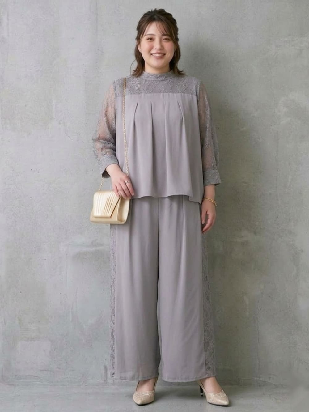 ゴールド系のバッグ、ベージュ系のパンプス、グレー系のパンツドレスを着用したレディースの秋コーディネートの2枚目の写真