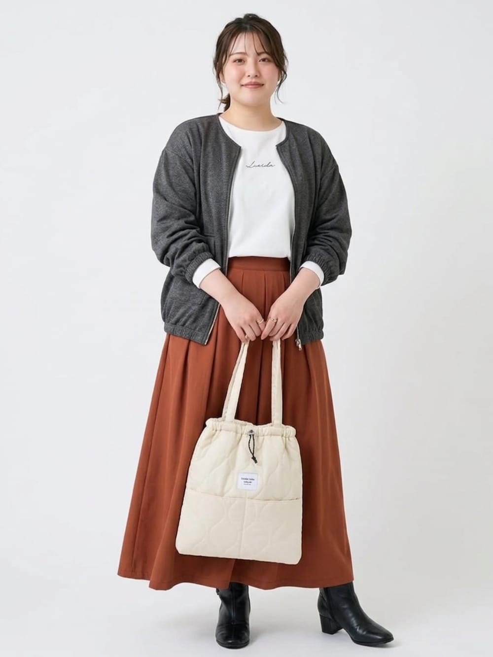 ブラウン系のスカート、ホワイト系のTシャツ/カットソー、ブラック系のブーツを着用したレディースの秋コーディネートの2枚目の写真
