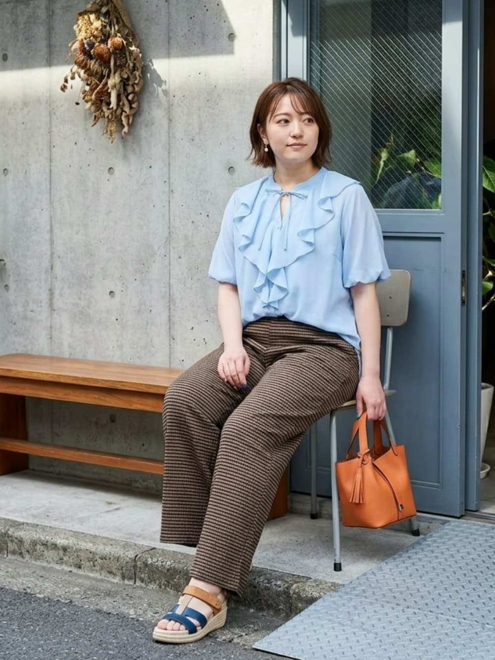 オレンジ系のトートバッグ、ブルー系のシャツ/ブラウス、ブラウン系のパンツを着用したレディースの夏コーディネートの3枚目の写真