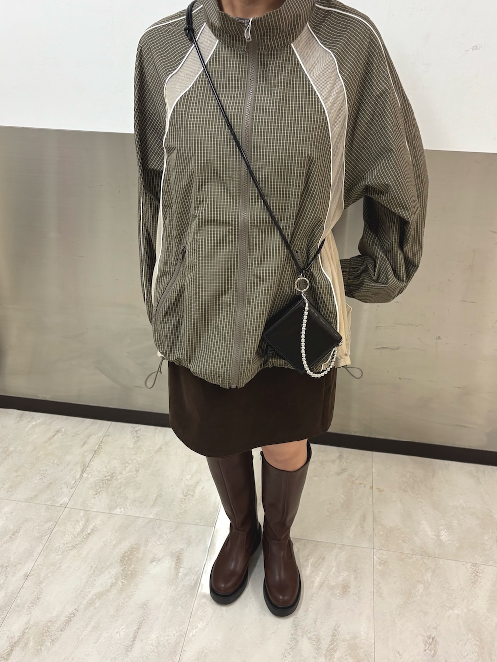 グリーン系のブルゾン、ブラウン系のスカート、ブラウン系のブーツを着用したレディースの秋コーディネートの4枚目の写真