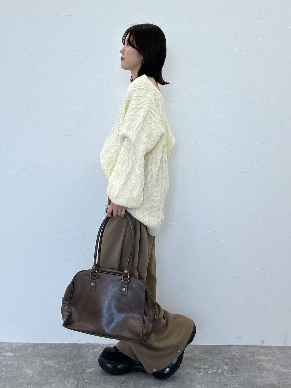 ブラウン系のボストンバッグ、ホワイト系のニット/セーター、ベージュ系のスラックスを着用したレディースの冬コーディネートの4枚目の写真