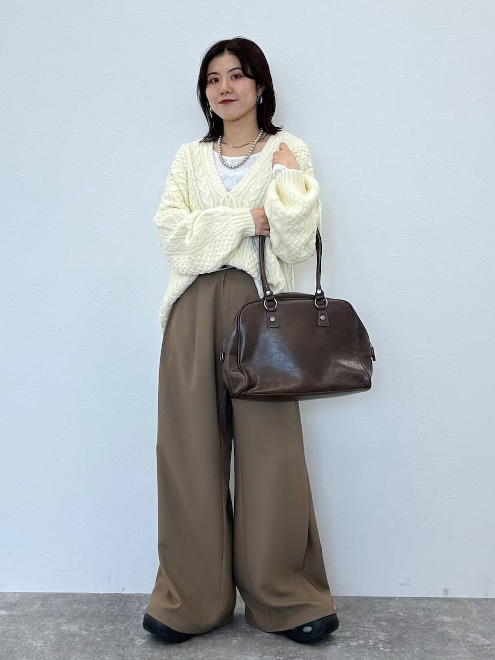 ブラウン系のボストンバッグ、ホワイト系のニット/セーター、ベージュ系のスラックスを着用したレディースの冬コーディネートの3枚目の写真