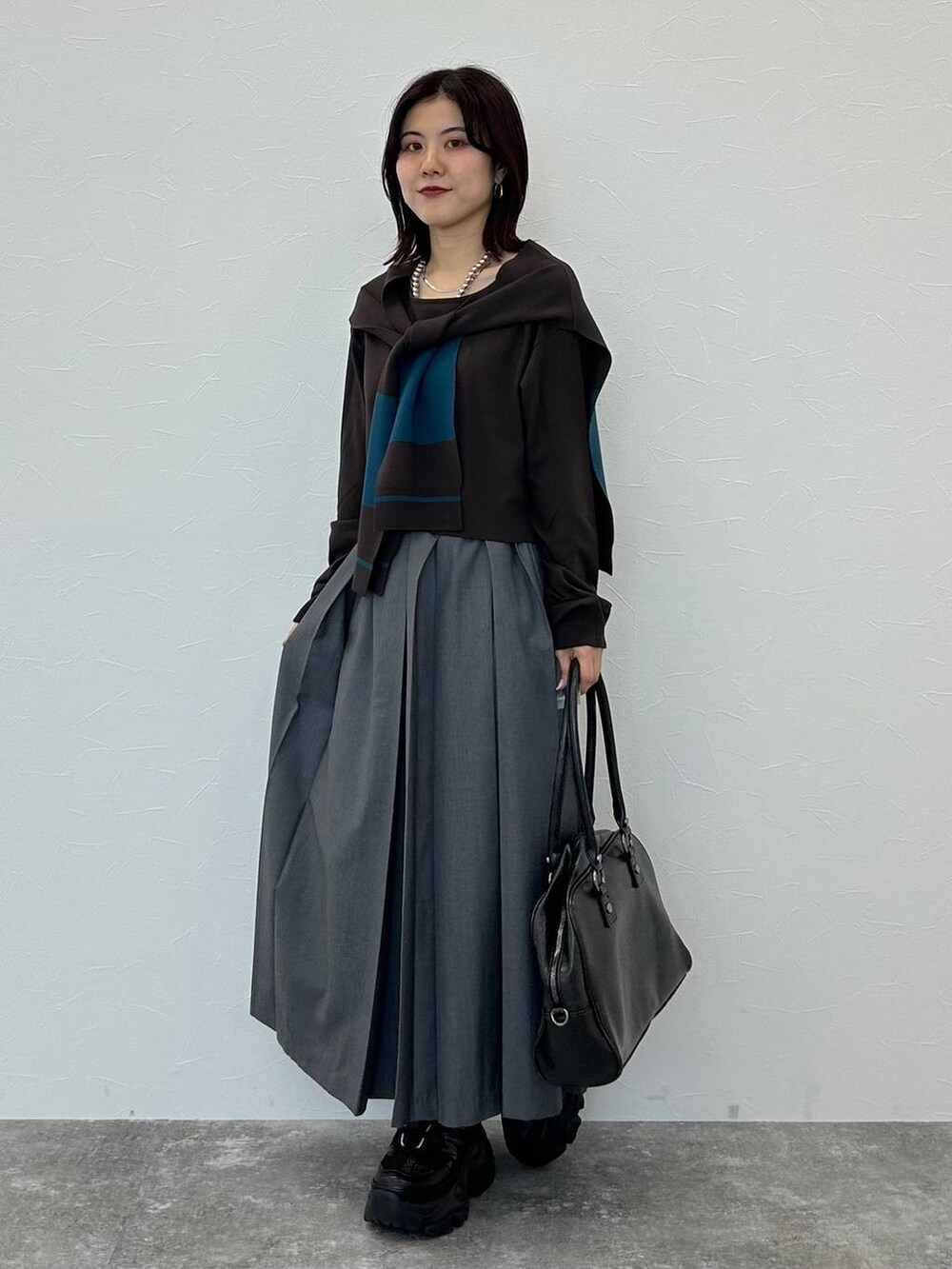ブラック系のスニーカー、グレー系のボストンバッグ、グレー系のスカートを着用したレディースの秋コーディネートの2枚目の写真
