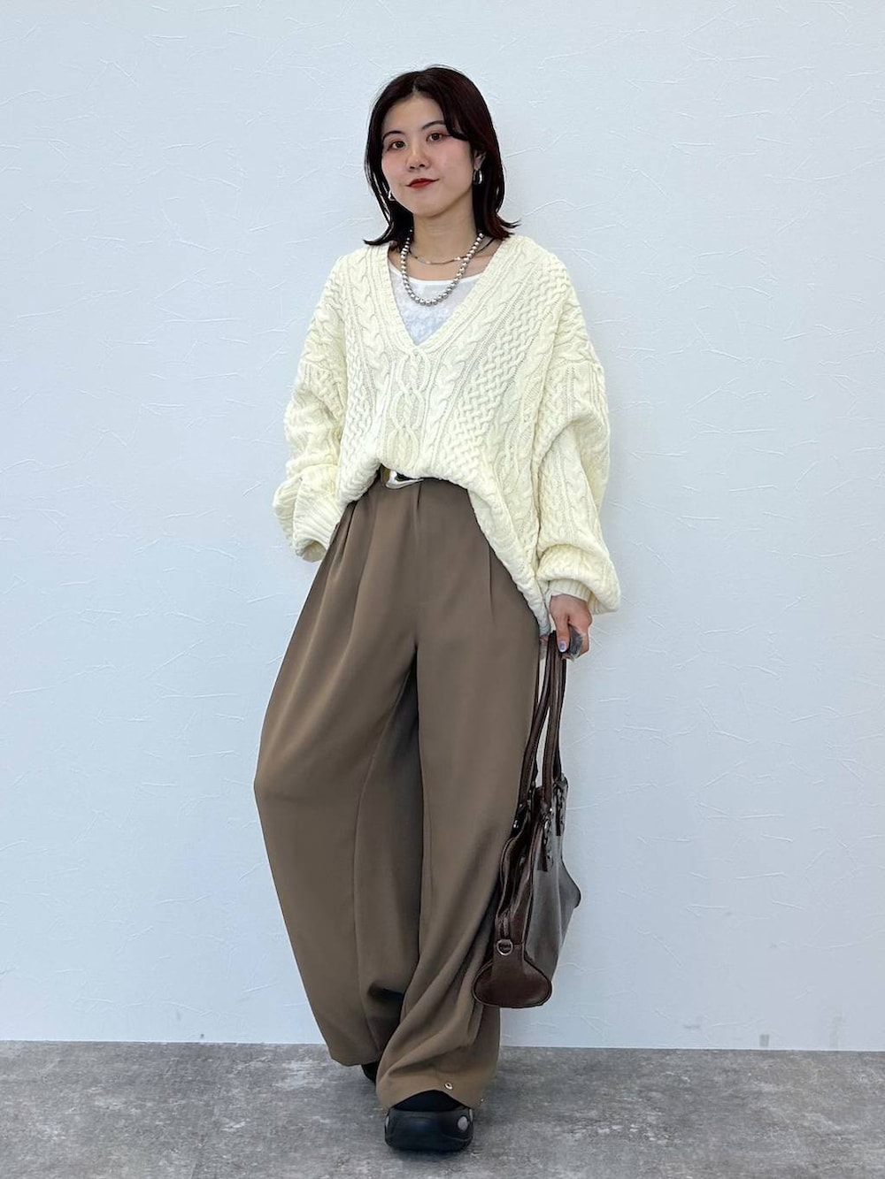ブラウン系のボストンバッグ、ホワイト系のニット/セーター、ベージュ系のスラックスを着用したレディースの冬コーディネートの2枚目の写真