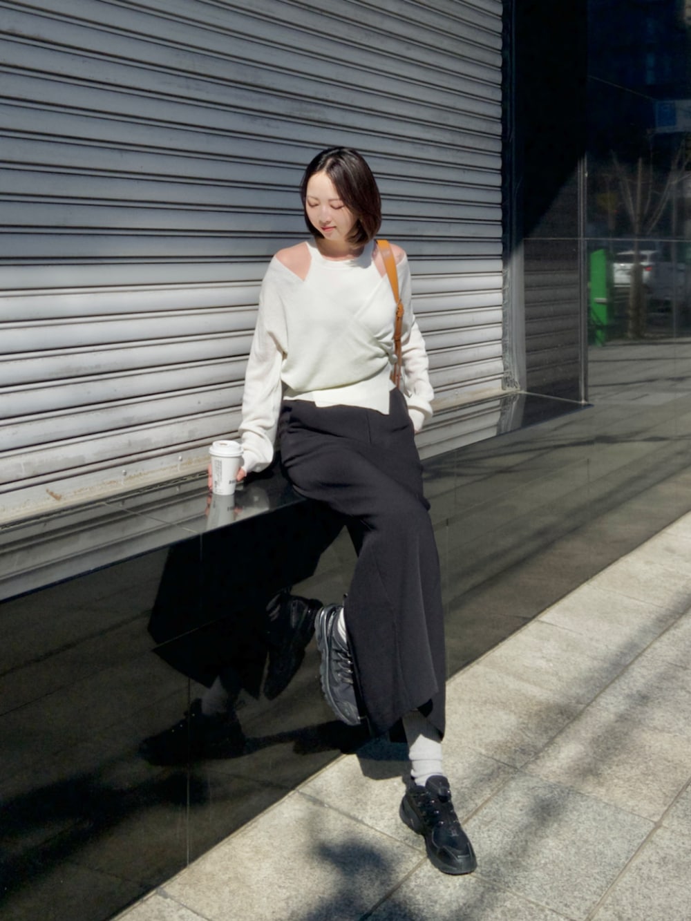 ブラック系のスカート、ベージュ系のショルダーバッグ、ホワイト系のカーディガン/ボレロを着用したレディースの春コーディネートの2枚目の写真