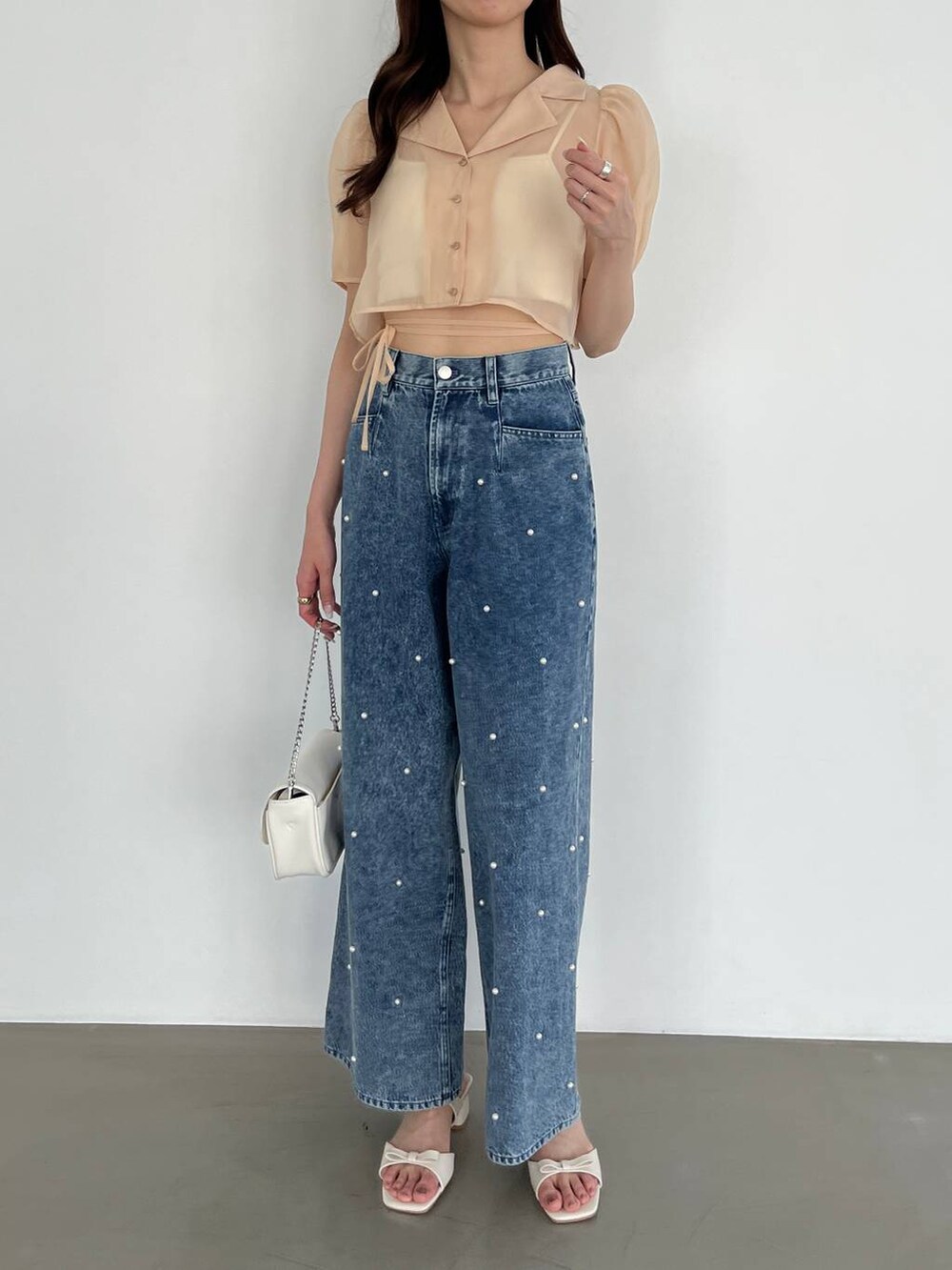 ホワイト系のショルダーバッグ、ブルー系のデニムパンツ、ホワイト系のキャミソールを着用したレディースの春コーディネートの3枚目の写真