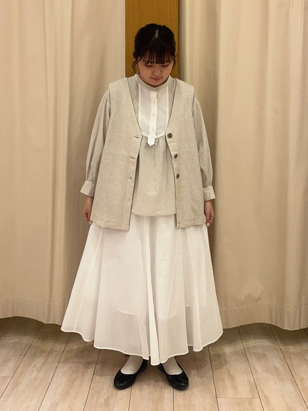 ホワイト系のスカート、ベージュ系のベストを着用したレディースの春コーディネートの2枚目の写真