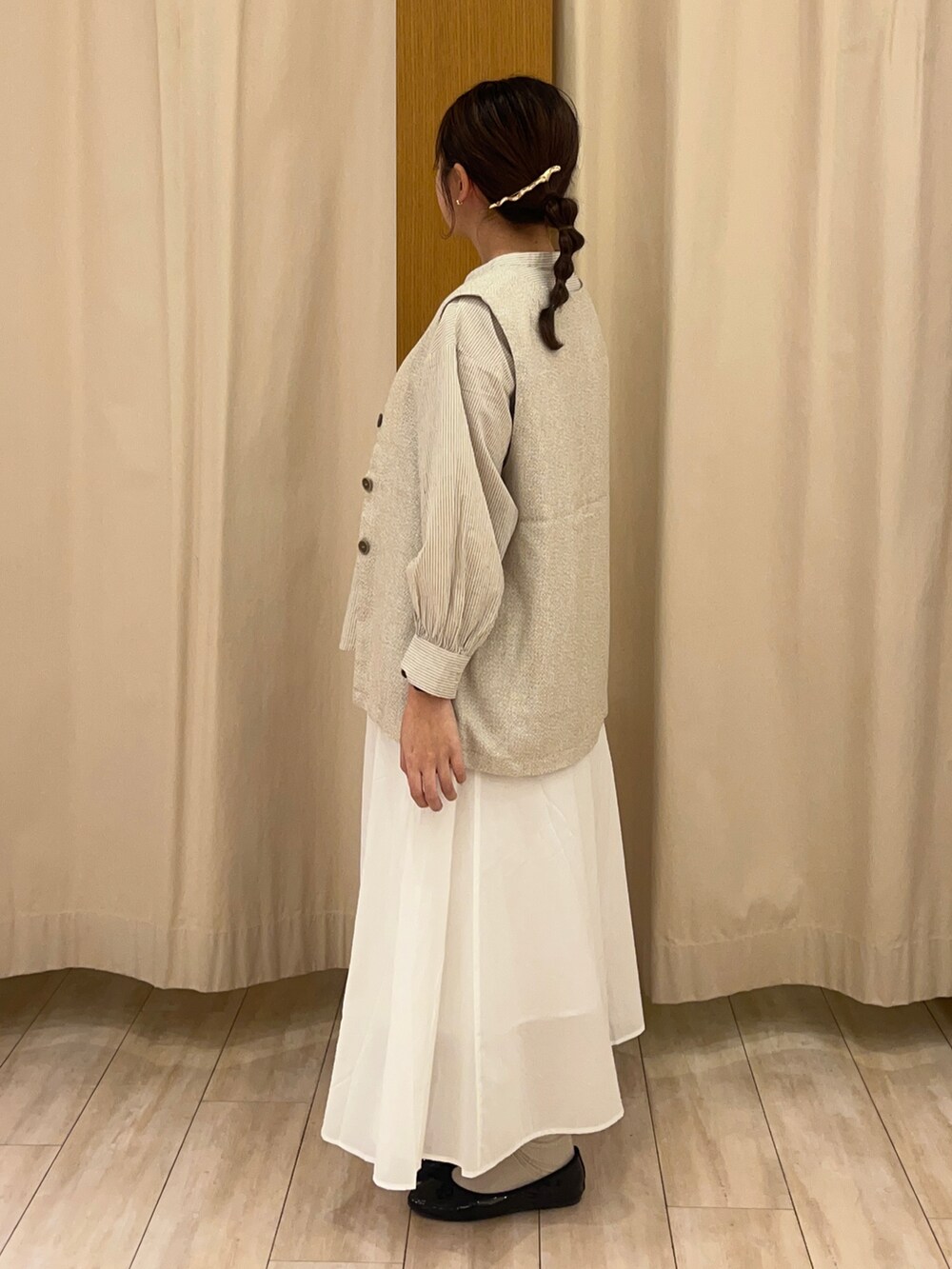 ホワイト系のスカート、ベージュ系のベストを着用したレディースの春コーディネートの3枚目の写真