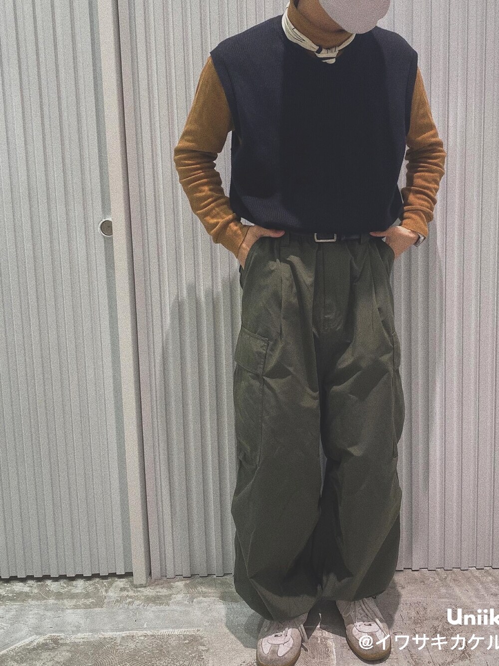 オレンジ系のTシャツ/カットソー、ブラック系のベスト、グリーン系のカーゴパンツを着用したメンズの春コーディネートの2枚目の写真