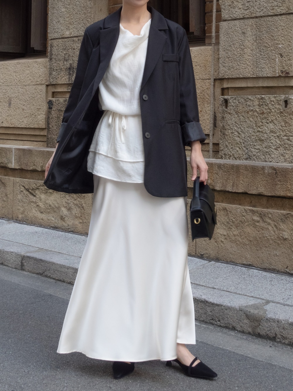 ブラック系のテーラードジャケット、ホワイト系のスカート、ブラック系のパンプスを着用したレディースの冬コーディネートの2枚目の写真
