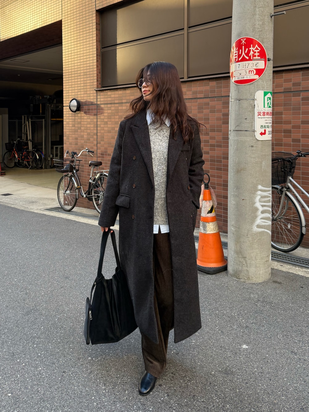 ブラック系のチェスターコート、ブラック系のトートバッグ、グレー系のニット/セーターを着用したレディースの秋コーディネートの2枚目の写真