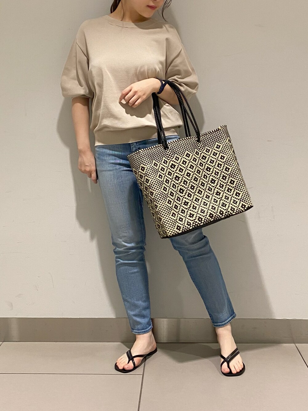 ブラック系のトートバッグ、ブルー系のニット/セーター、ブルー系のデニムパンツを着用したレディースの春コーディネートの2枚目の写真