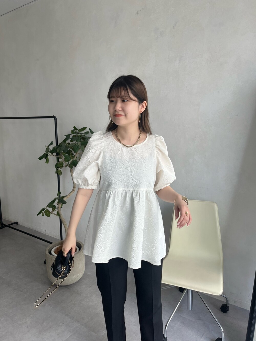 ブラック系のショルダーバッグ、ホワイト系のパンツドレス、ゴールド系のネックレスを着用したレディースの春コーディネートの3枚目の写真