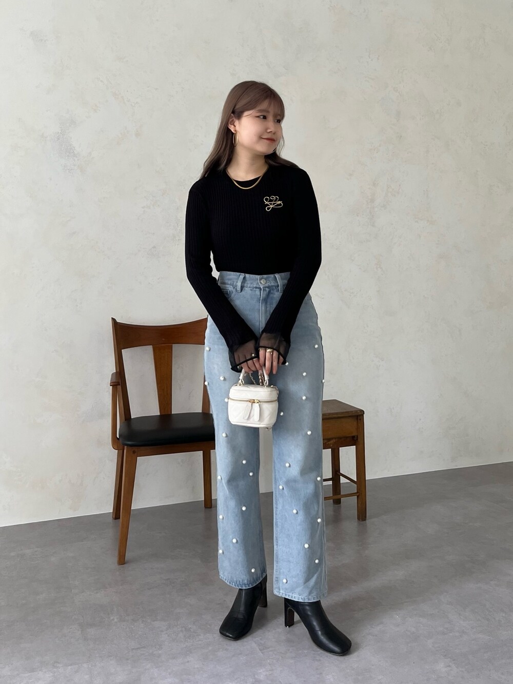 ブラック系のニット/セーター、ブルー系のデニムパンツ、ゴールド系のブローチ/コサージュを着用したレディースの夏コーディネートの2枚目の写真