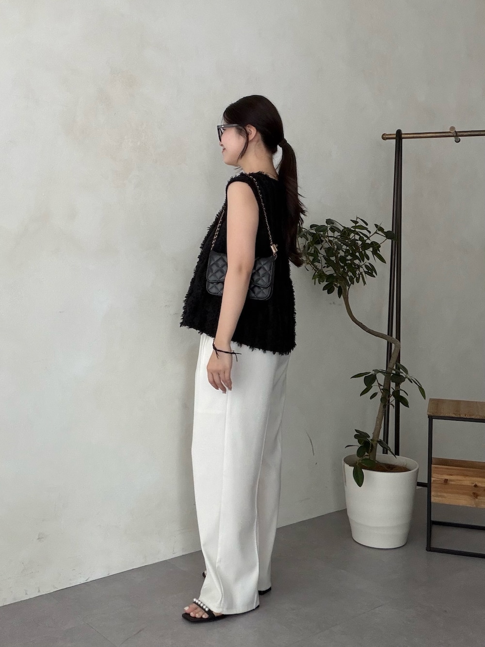 ブラック系のトートバッグ、ホワイト系のスラックス、ブラック系のサンダルを着用したレディースの夏コーディネートの2枚目の写真
