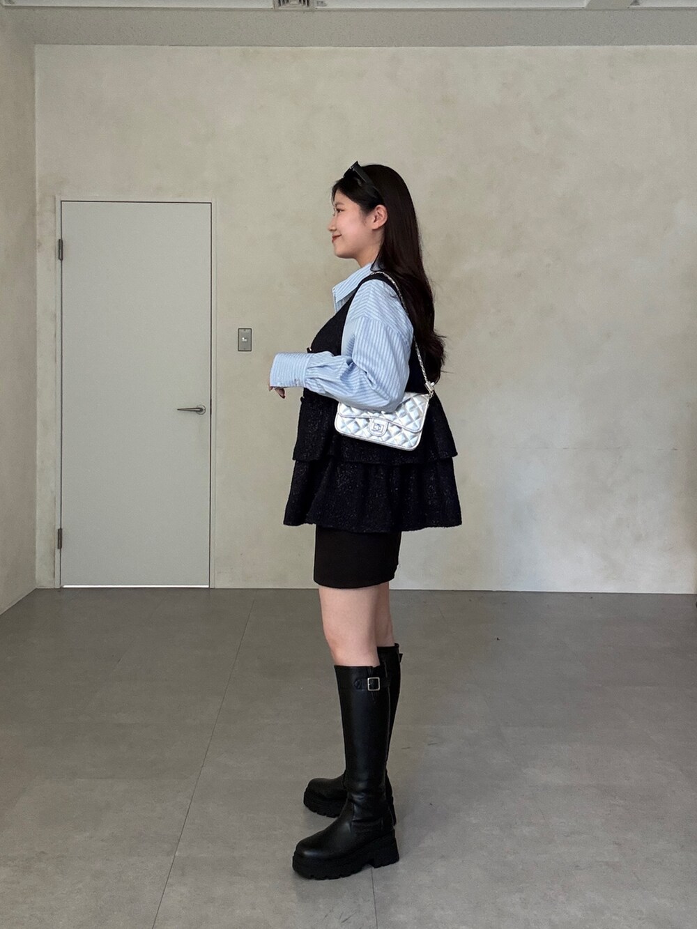 ブラック系のスカート、ブラック系のブーツ、ブルー系のベストを着用したレディースの冬コーディネートの2枚目の写真