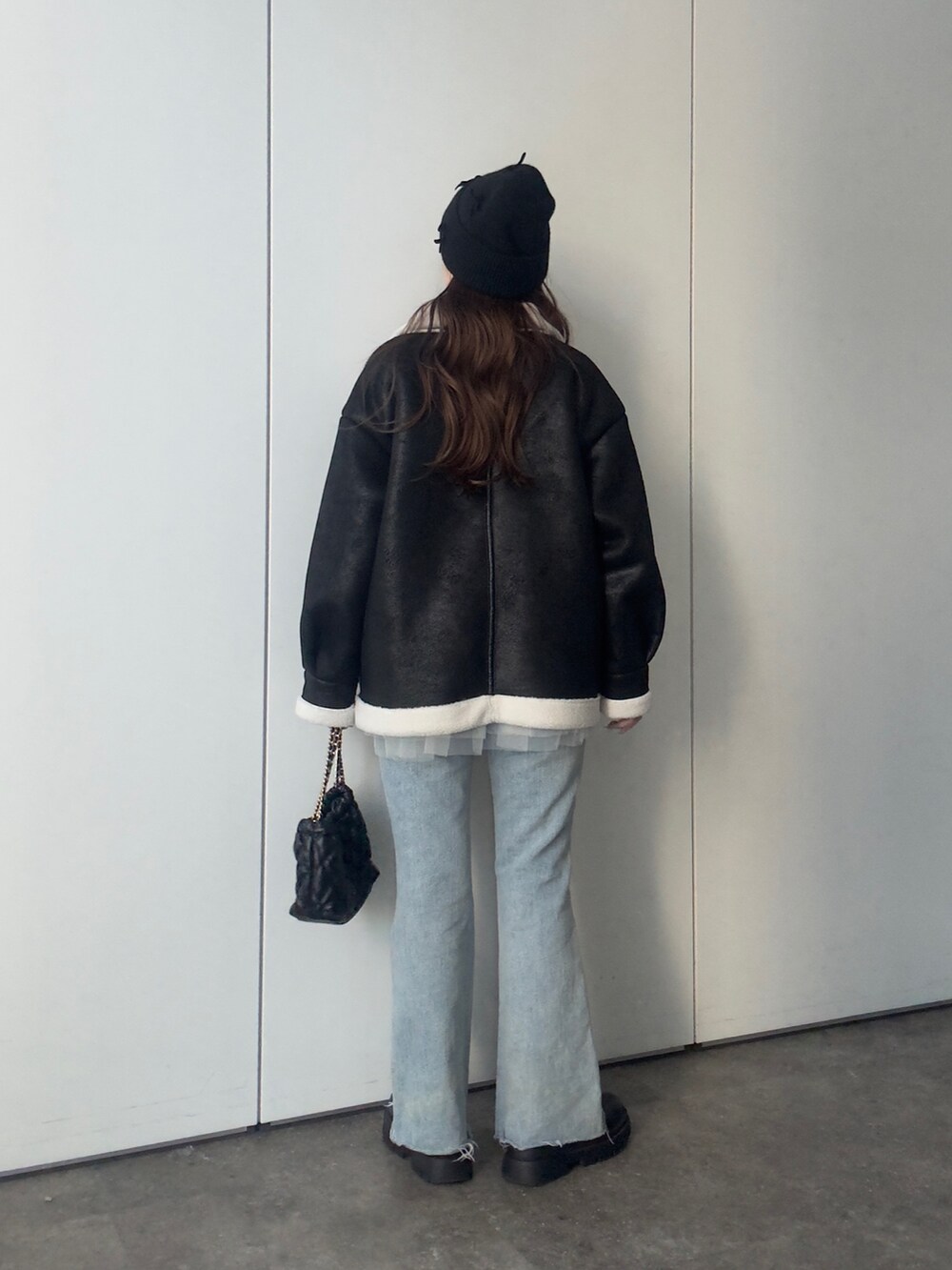 ブラック系のムートンコート、ホワイト系のニット/セーター、ブルー系のデニムパンツを着用したレディースの冬コーディネートの3枚目の写真
