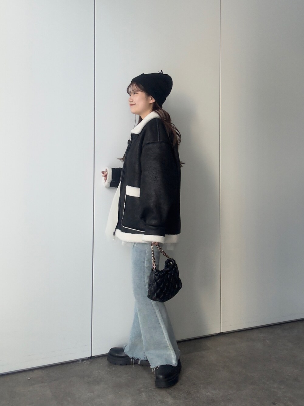 ブラック系のムートンコート、ホワイト系のニット/セーター、ブルー系のデニムパンツを着用したレディースの冬コーディネートの2枚目の写真
